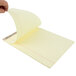 A hand holding a TOPS Second Nature yellow lined legal pad.