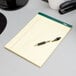 A pen on a TOPS narrow ruled canary writing pad.