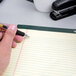 A hand holding a pen writing on a TOPS narrow ruled writing tablet.