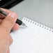 A hand holding a pen writes on a white wirebound Gregg ruled steno pad.