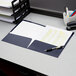 A navy blue Oxford laminated paper pocket folder on a desk with a stack of papers and a pen in a white mug.