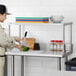 A man in a white shirt and black pants cutting vegetables on a table with a Regency stainless steel overshelf.