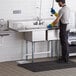 A person wearing gloves standing next to a Regency 2 compartment sink in a kitchen.