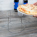 A hand holding a pizza on a Choice chrome plated steel display stand.