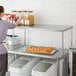 A woman standing in a professional kitchen using a Regency stainless steel single deck overshelf.