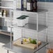 A Regency stainless steel double deck overshelf on a counter over a table with food items on it.