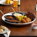 An aluminum Choice tray with ribs, corn, and other food on it.