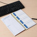 An Adams Write 'n Stick phone message notebook with a spiral bound page on a desk with a pen and keyboard.