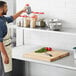 A man in an apron standing in a professional kitchen with a Regency stainless steel table mounted overshelf.