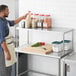 A man in an apron standing next to a Regency stainless steel table mounted overshelf.