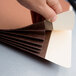 A hand cutting a brown Pendaflex heavy-duty file pocket with a knife.