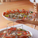 A person holding a platter of seafood including crab legs, limes, and sauces on a Choice aluminum tray.