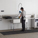 A man wearing gloves and an apron washing dishes in a Regency two compartment sink with drainboards in a professional kitchen.