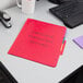 A red Pendaflex folder with a fastener on a desk.