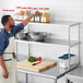 A man in an apron standing in a professional kitchen in front of a Regency stainless steel double deck overshelf.