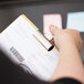 A hand using an X-Acto Bulldog Clip to hold papers on a clipboard.