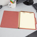 A red Pendaflex classification folder with lined paper inside on a desk.