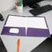 A purple Oxford pocket folder on a desk with pens in a white cup.