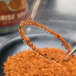 A spoon with Twang-a-Rita Sunrise Spice Chili-Lime Rimming Salt on the rim of a glass.