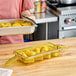 A woman using a Cambro 1/3 size amber plastic food pan with double handles to serve corn on the cob.