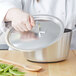 A person holding a Vollrath aluminum lid over a pot.