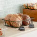 A counter with bread rolls in black wire pastry baskets.