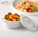 A white Bon Chef porcelain cocotte with a lid filled with food.