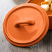 The lid for a small orange porcelain oval cocotte.