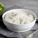 A white porcelain bowl filled with rice on a table with silverware.