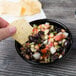 A person holding a chip over a black bowl of food.