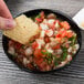 A person holding a chip over a bowl of salsa.