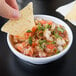 A person holding a chip dipping it into a white Thunder Group Melamine salsa dish.