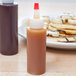 A Tablecraft Chef squeeze bottle filled with syrup next to a plate of pancakes.