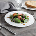 A Bon Chef white bone china salad plate with a fork and knife next to a salad with strawberries and cheese.