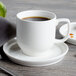 A white cup of coffee sits on a white saucer.