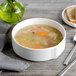 A white porcelain soup bowl filled with soup, with a spoon and a piece of bread on the table.