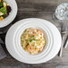 A white porcelain oval pasta bowl with pasta and salad on it.