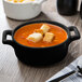 A matte black porcelain oval cocotte filled with soup and croutons.