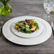 A Bon Chef white porcelain round salad plate with salad on a table.