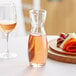 A Libbey glass carafe filled with pink liquid on a table next to a glass of the same liquid.