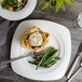 A white Bon Chef soft square porcelain dinner plate with food on it.