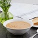 A white porcelain bowl of soup with a spoon on a table.