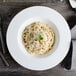 A close up of a Bon Chef white bone china pasta plate with pasta and a fork on it.