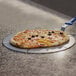 A pizza being cut on a GI Metal pizza pan with a blue handle.