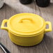 A yellow Bon Chef porcelain oval cocotte with a handle on a table.