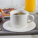 A white cup of coffee on a white saucer.