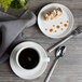 A white porcelain plate with food and a cup of coffee on a table.