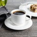 A Bon Chef white porcelain espresso cup on a saucer with coffee and food.