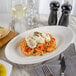 A white Bon Chef porcelain plate with pasta, shrimp, and sauce on it on a table with a glass of white wine.