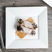 A Bon Chef white bone china square plate with food on a wood table.